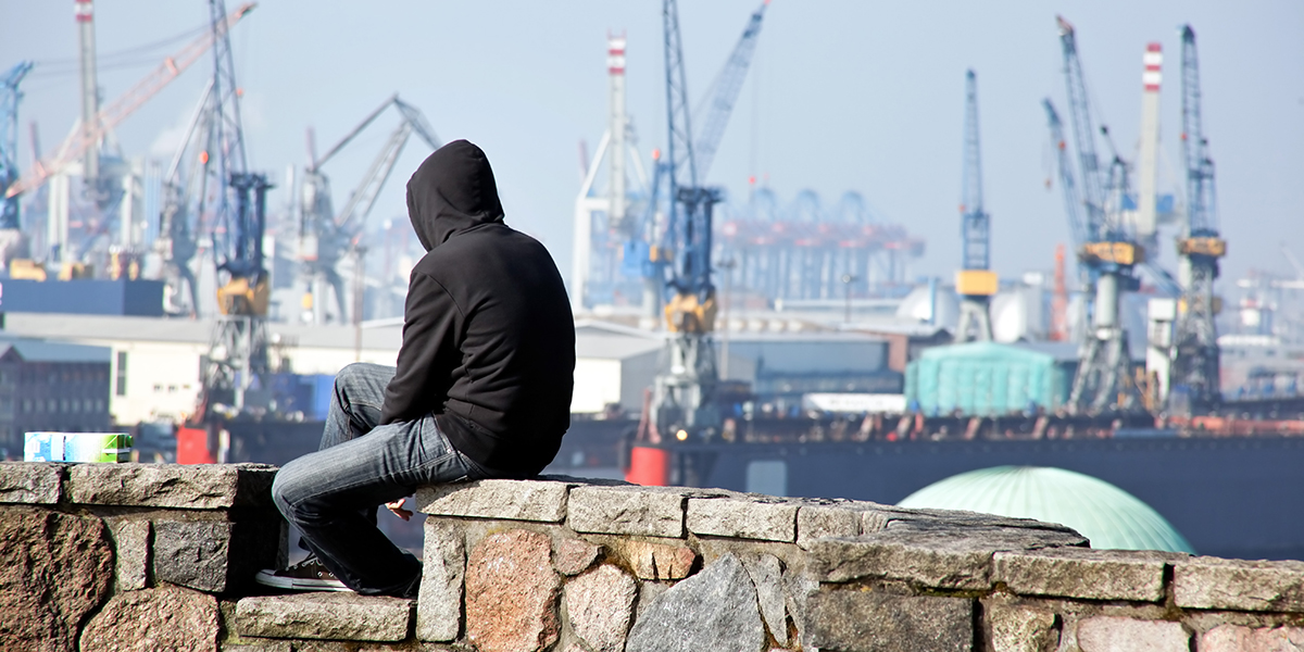 A young man using a hoodie and looking at the harbor