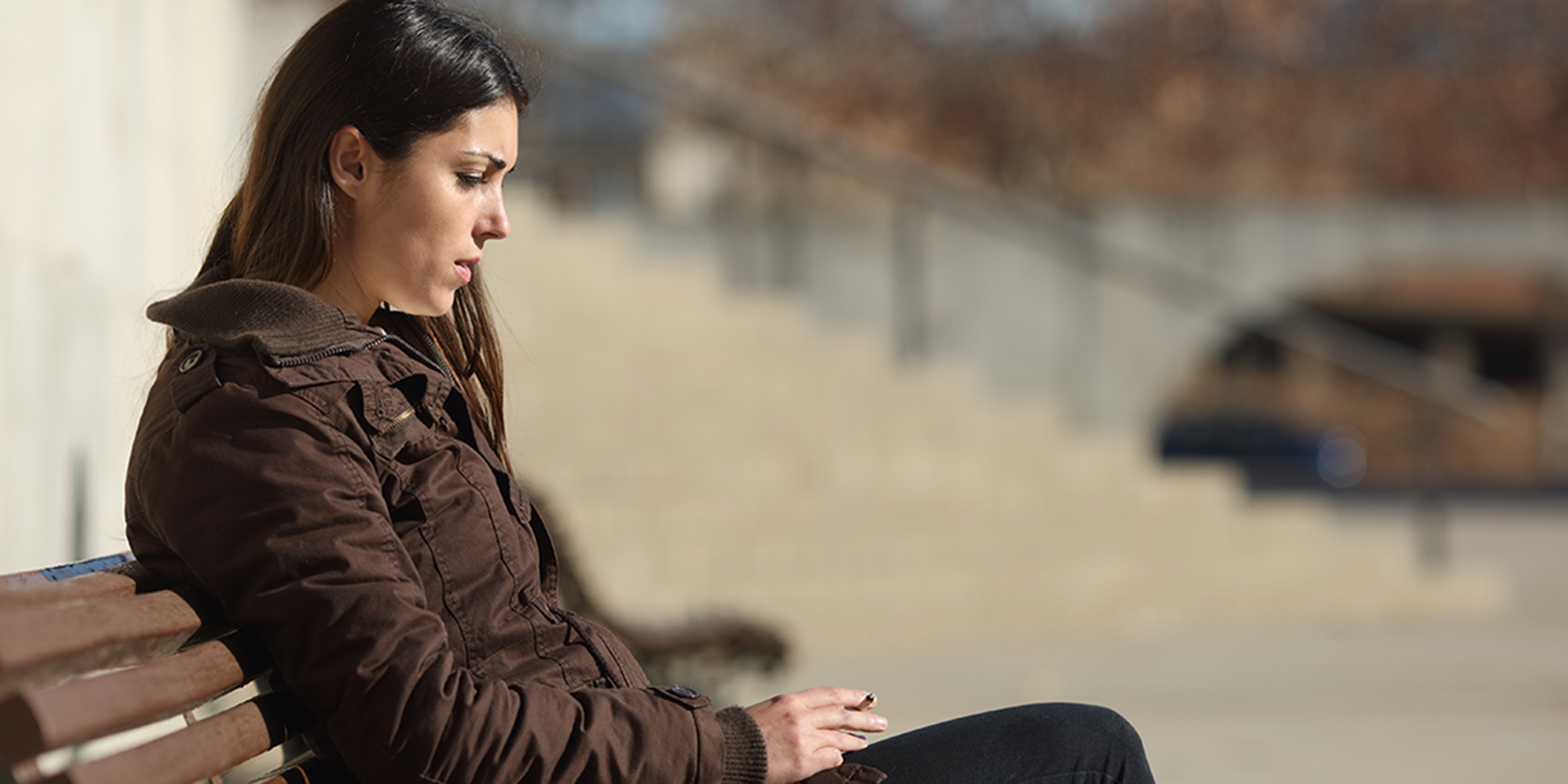 Serious young woman sitting on a bench outdoors